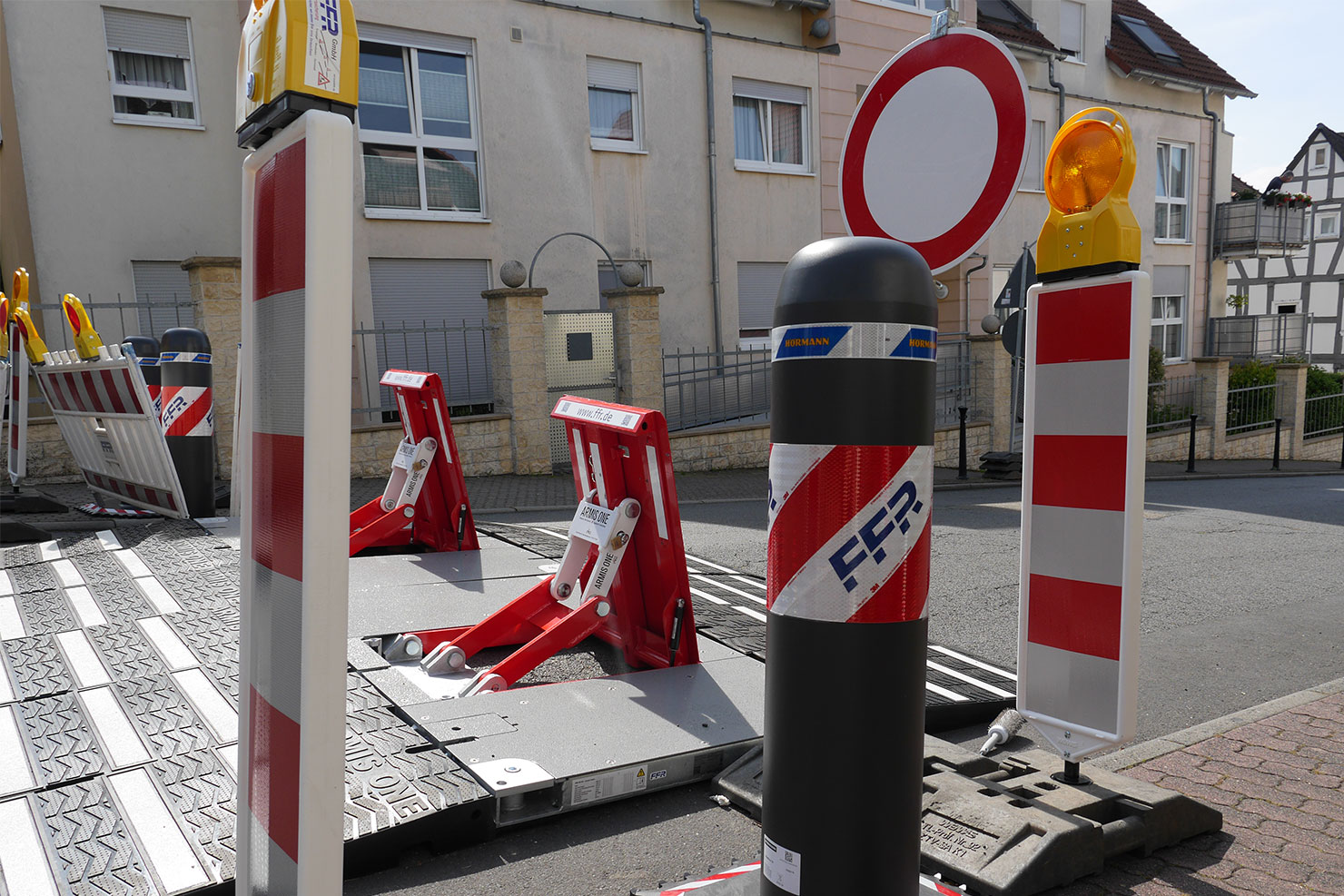 Fahrzeugsperren der Arten ARMIS ONE und OktaBlock TR stehen umgeben von Leitbaken auf einer Straße.