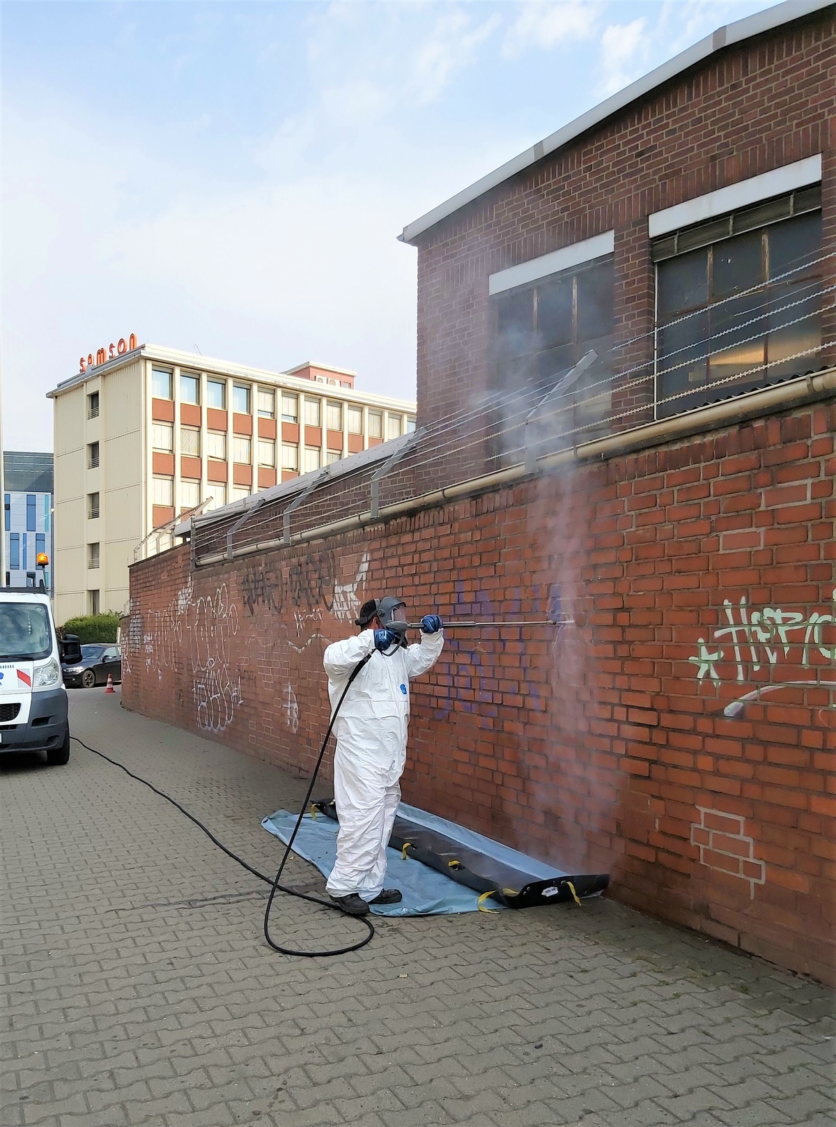Mitarbeiter in Schutzkleidung entfernt mit einem Hochdruckreiniger ein Graffiti