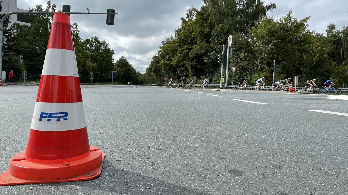Leitkegel an einer Straße, im Hintergrund vorbeifahrende Rennradfahrer