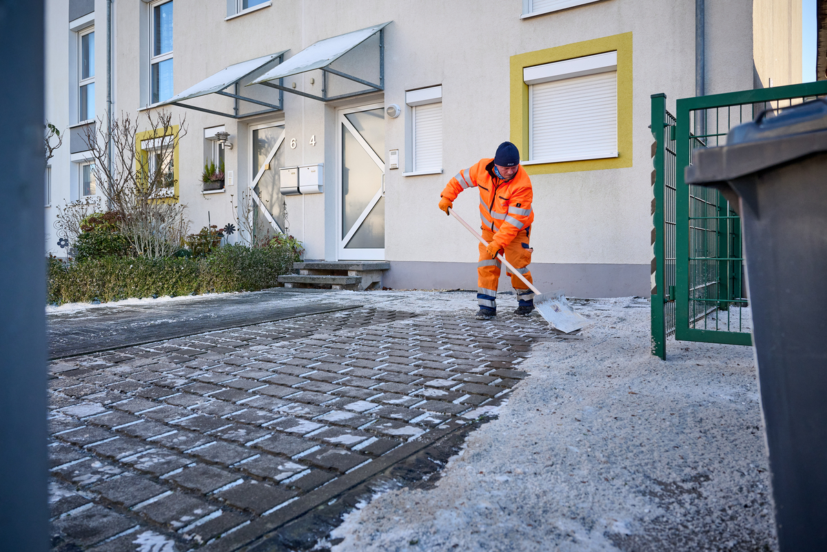 FFR-Mitarbeiter schippt Schnee vor einem Mehrfamilienhaus