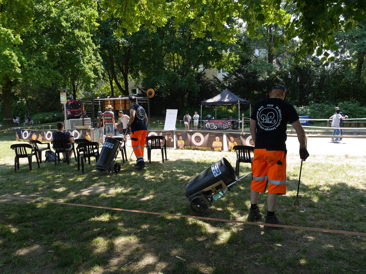 Mitarbeiter mit Mülltonnen und Greifern sammeln Müll bei einer Veranstaltung