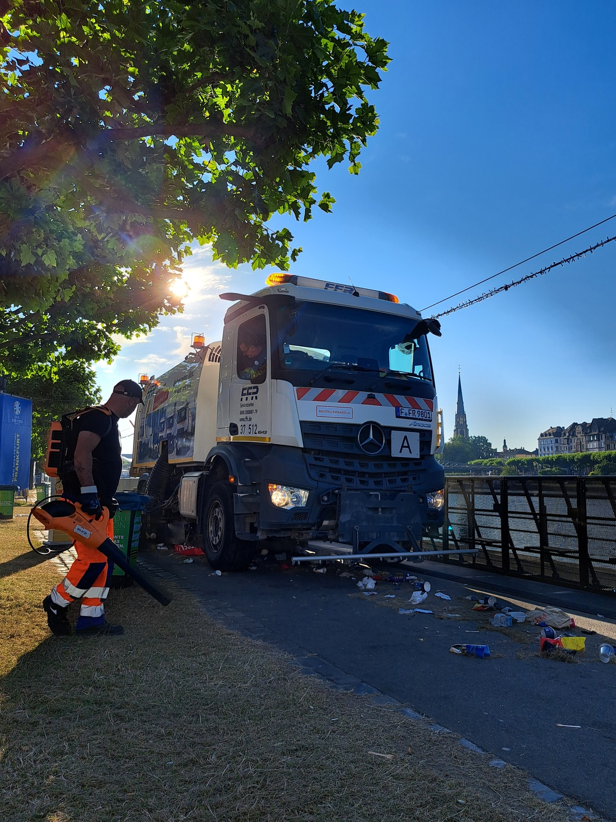 Reinigungsfahrzeug und Mitarbeiter mit Laubbläser reinigen nach einer Veranstaltung